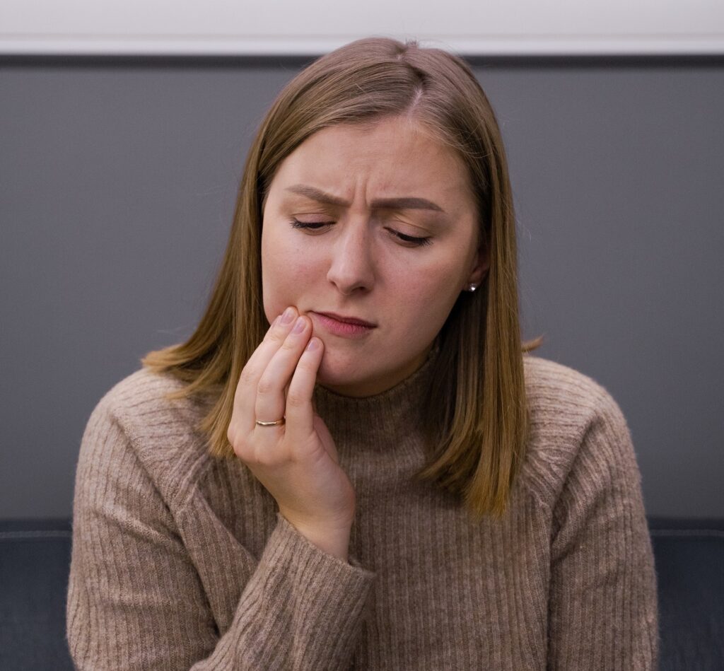 Woman with toothache. She is holding the right side of her mouth and looks in pain